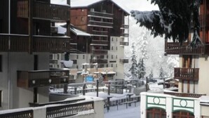Ein verschneites Skigebiet mit mehrstöckigen Gebäuden, Balkonen und einer Brücke.