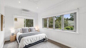 A bedroom with a large window, a bed with striped bedding, and a small bedside table with a lamp. - Botanic Breeze on Lindsay! (East Toowoomba)