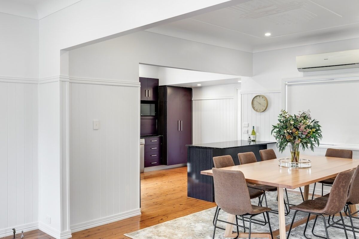 A modern kitchen with white walls, dark cabinets, and a wooden dining table with chairs.