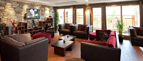 A spacious lobby with a stone wall, a flat-screen TV, multiple seating areas, and large windows offering a view of the outdoors.