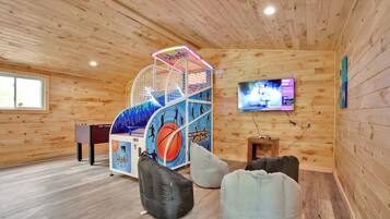 A wooden interior with a basketball arcade, bean bags, and a TV on the wall.