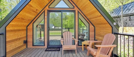 A wooden cabin with a sloped roof, a deck with two Adirondack chairs, and a glass door entrance.