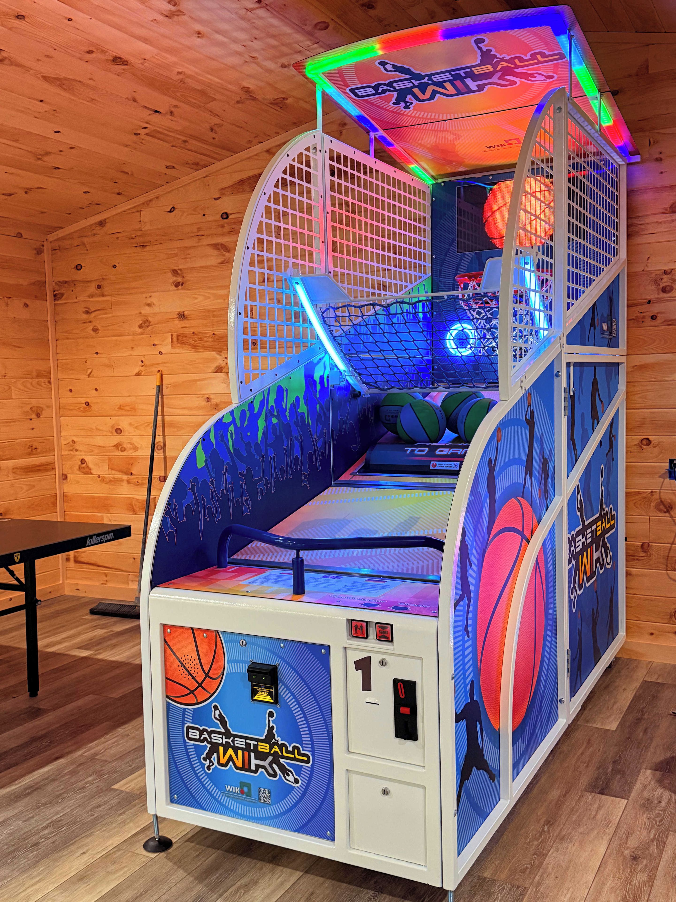 Un jeu d’arcade de basket-ball avec un intérieur en bois et une table située à gauche.