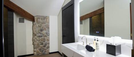 Une salle de bain moderne avec un mur d’accent en pierre, un grand miroir et un lavabo en marbre blanc.