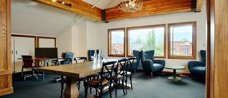 A conference room with a wooden table, chairs, and a chandelier. There are windows with a view of buildings and trees.