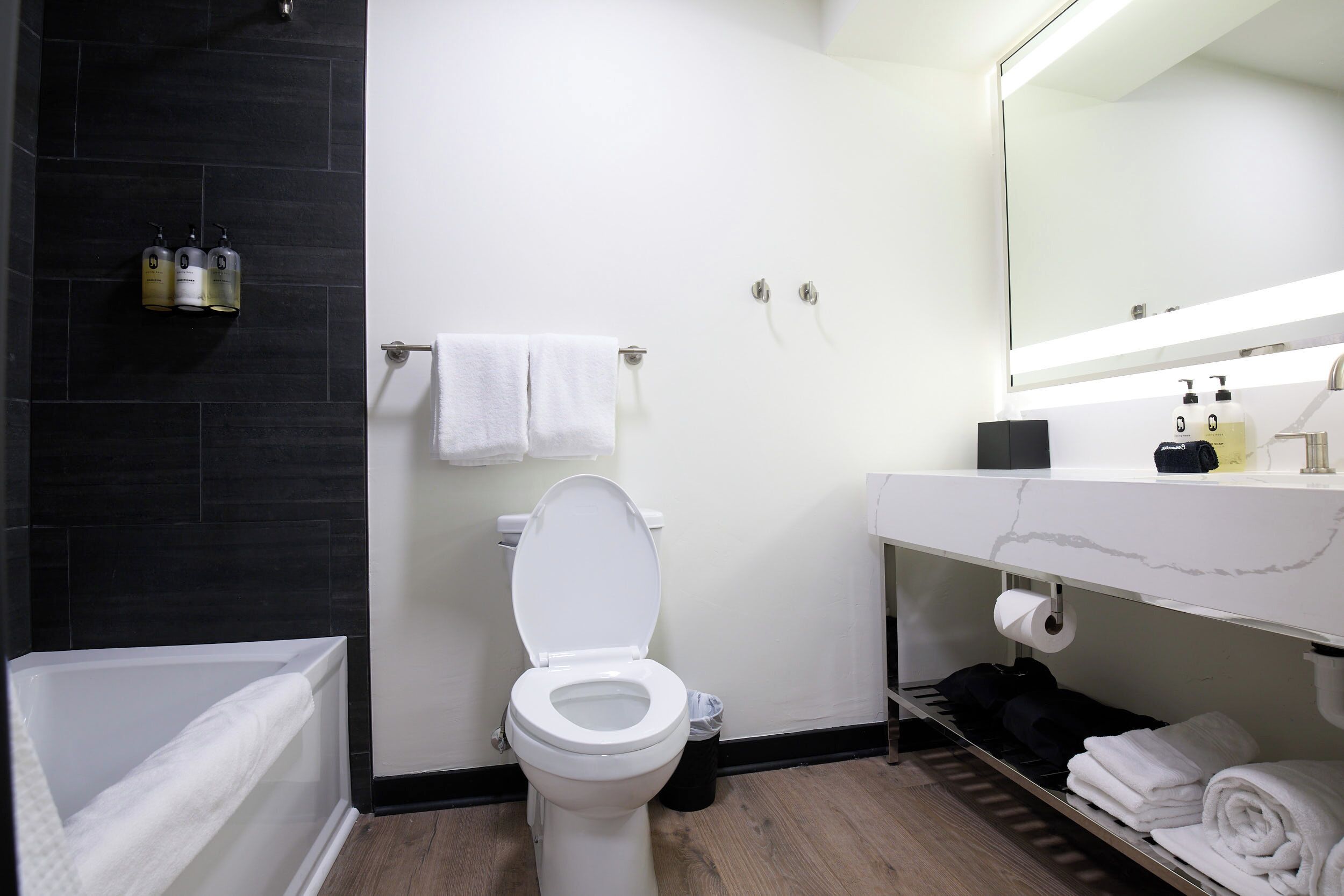 Ein modernes Badezimmer mit einer weißen Toilette, einem schwarzen Duschbereich mit Fliesen, einem weißen Waschbecken mit Marmorplatte und einem großen Spiegel darüber.