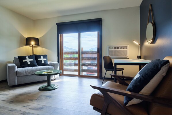 A modern living room with a sofa, armchair, and a small table. There is a large window with a view of the outdoors. - Gravity Haus Big Sky (Big Sky)