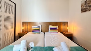 A hotel room with two beds, each with a striped pillow, wooden headboard, and bedside lamps.