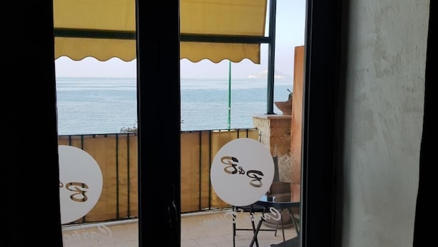 A balcony with a view of the sea, featuring two round tables with a logo. - Hotel Taromy  (Naples)