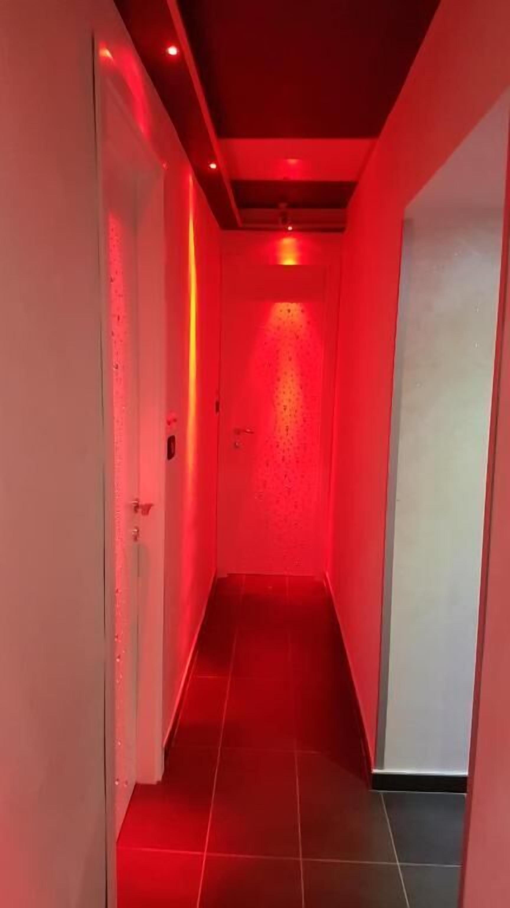 A narrow hallway with red lighting, tiled floor, and white walls.
