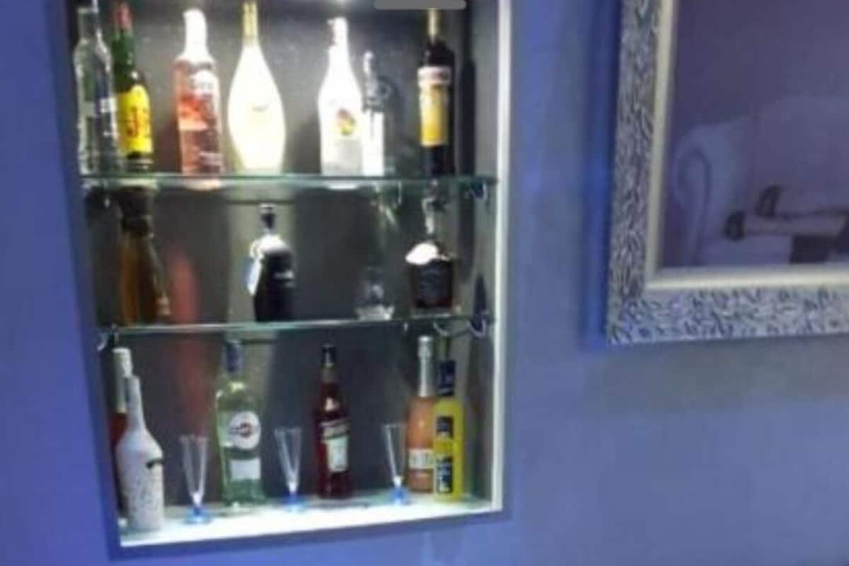 Ein Zimmer mit einer schwarzen Ledersofa, einer Vitrine mit verschiedenen Flaschen, einem kleinen Tisch mit einer Lampe und einem gerahmten Bild an der Wand.
