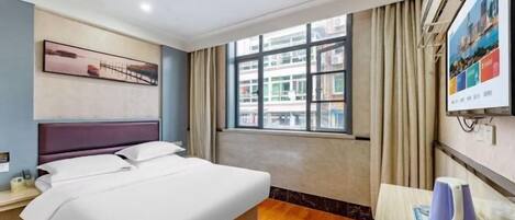 A hotel room with a bed, a desk, a kettle, and a window with curtains.