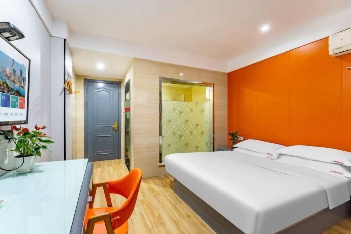 Une chambre d’hôtel comprenant un lit, un bureau avec une chaise, une petite table avec une plante et une porte donnant sur une salle de bain.