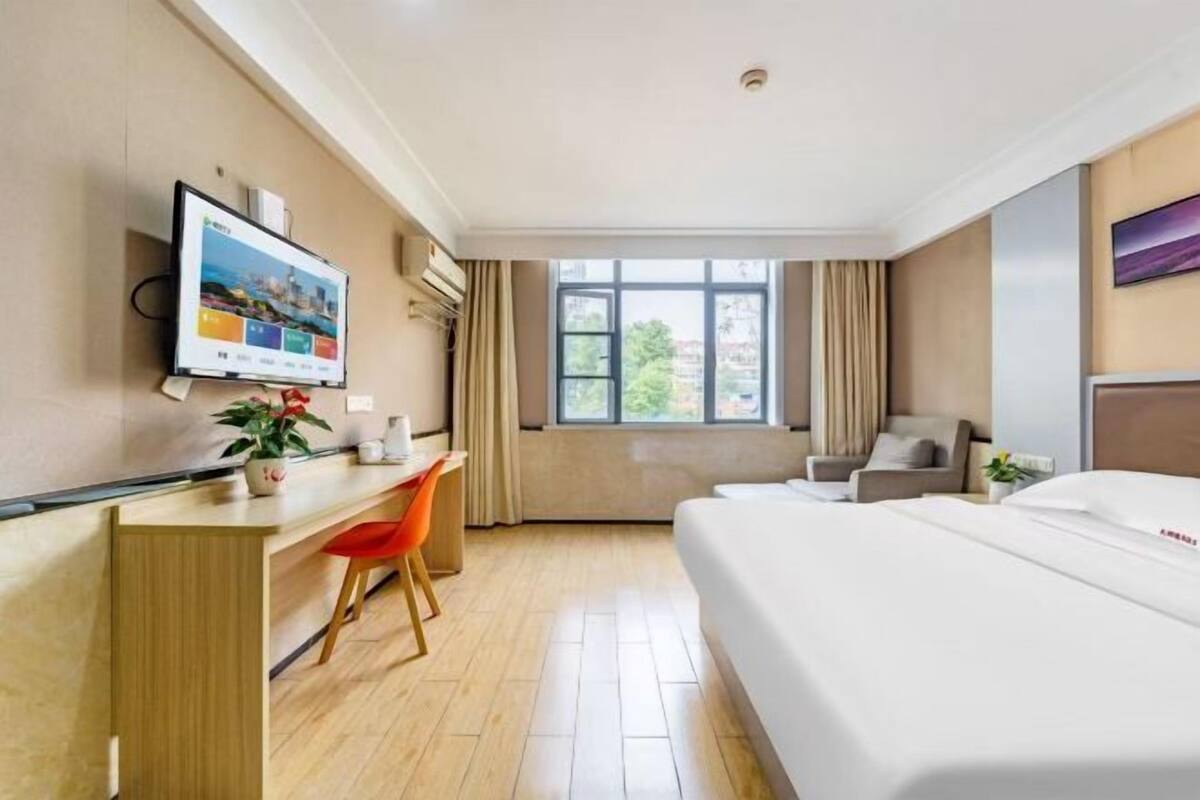Une chambre d’hôtel comprenant un lit, un bureau avec une chaise, un téléviseur fixé au mur et une fenêtre avec des rideaux.