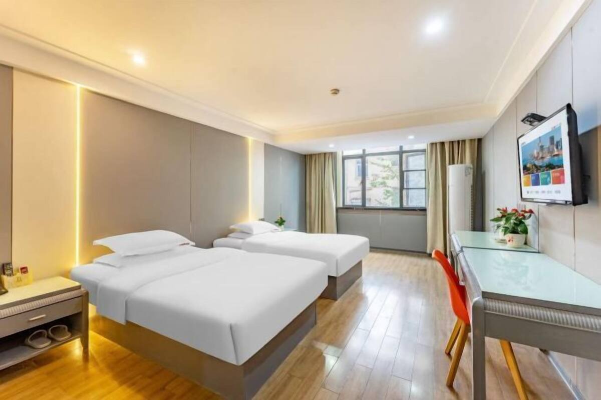 Une chambre d’hôtel avec deux lits, un bureau, une chaise, une télévision et une fenêtre avec des rideaux.