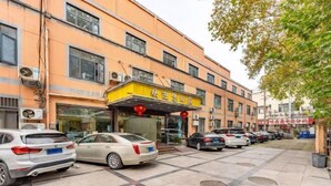 A multi-story building with a yellow facade and several parked cars in front. - Tianhu Hotel (Nanjing)