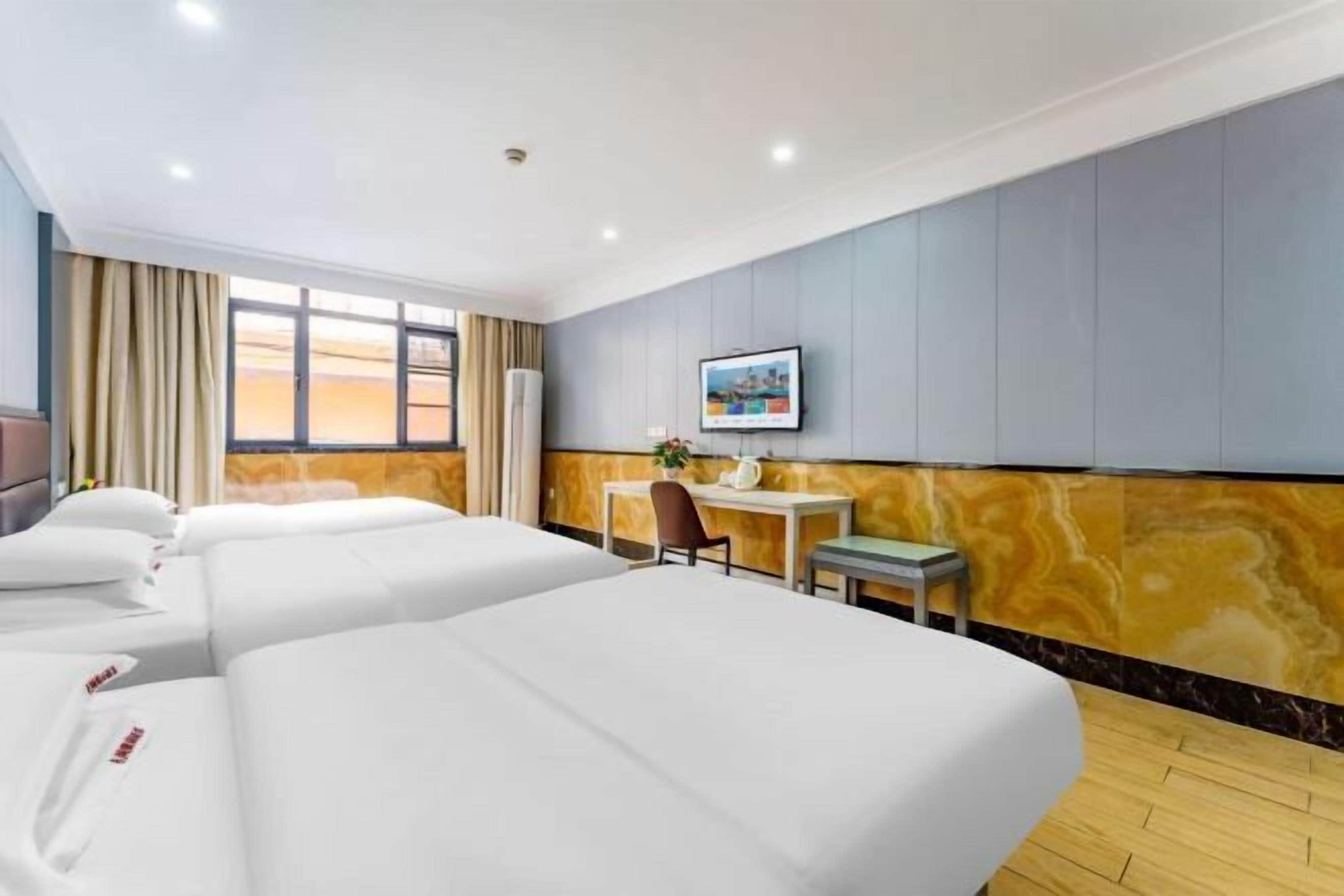 A hotel room with three beds, a desk, a chair, a TV, and a window with curtains.