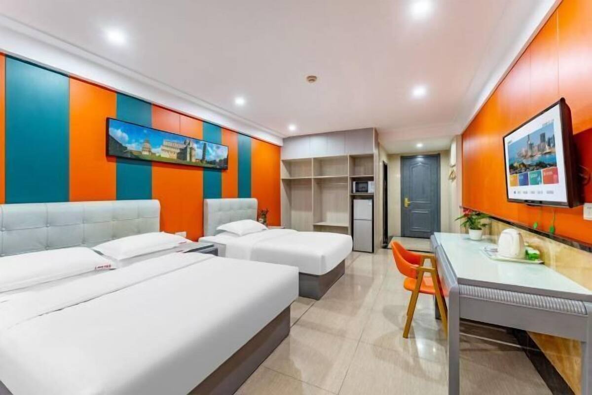 Une chambre d’hôtel avec deux lits, un bureau et une chaise. Il y a un téléviseur accroché au mur et une porte qui donne sur une autre pièce.