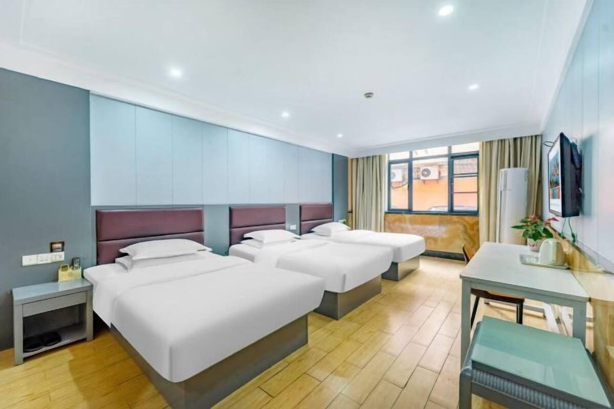 Une chambre d’hôtel avec trois lits, un bureau, une chaise, une télévision et une fenêtre avec des rideaux.