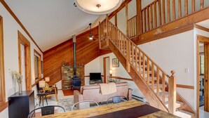 A spacious living area with a high ceiling, wooden staircase, and a fireplace.