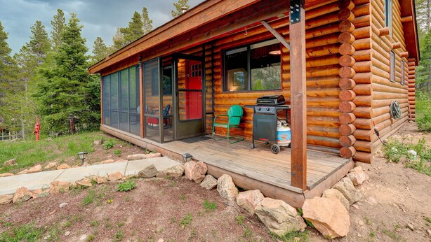 A log cabin with a deck, sliding glass doors, and a barbecue grill.