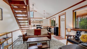 A spacious living area with a staircase, a sofa, a coffee table, and a kitchen area.