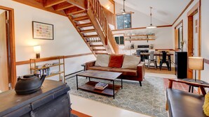 A cozy living room with a wooden staircase, a sofa, a coffee table, and a bookshelf.
