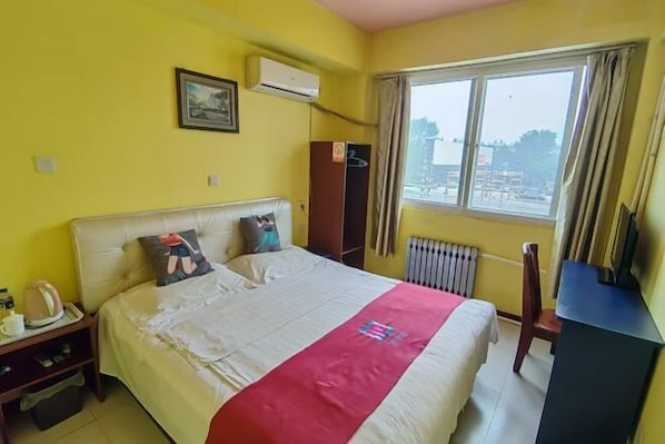A hotel room with a bed, a desk, a radiator, and a window with curtains.