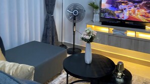 Una sala de estar con un sofá, un televisor, un ventilador y un jarrón decorativo.