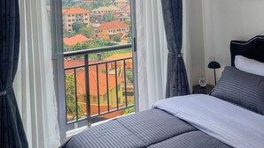 Una habitación de hotel con un ventanal grande, una cama, una mesita de noche y un cuadro en la pared.