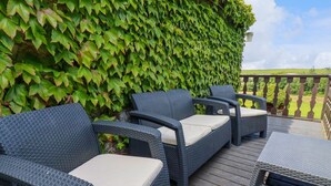 A deck with wicker furniture and a green ivy-covered wall. - Hollies Cottage (Truro)