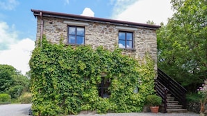 A stone house with a gravel driveway and a wooden staircase leading to the entrance. - Hollies Cottage (Truro)