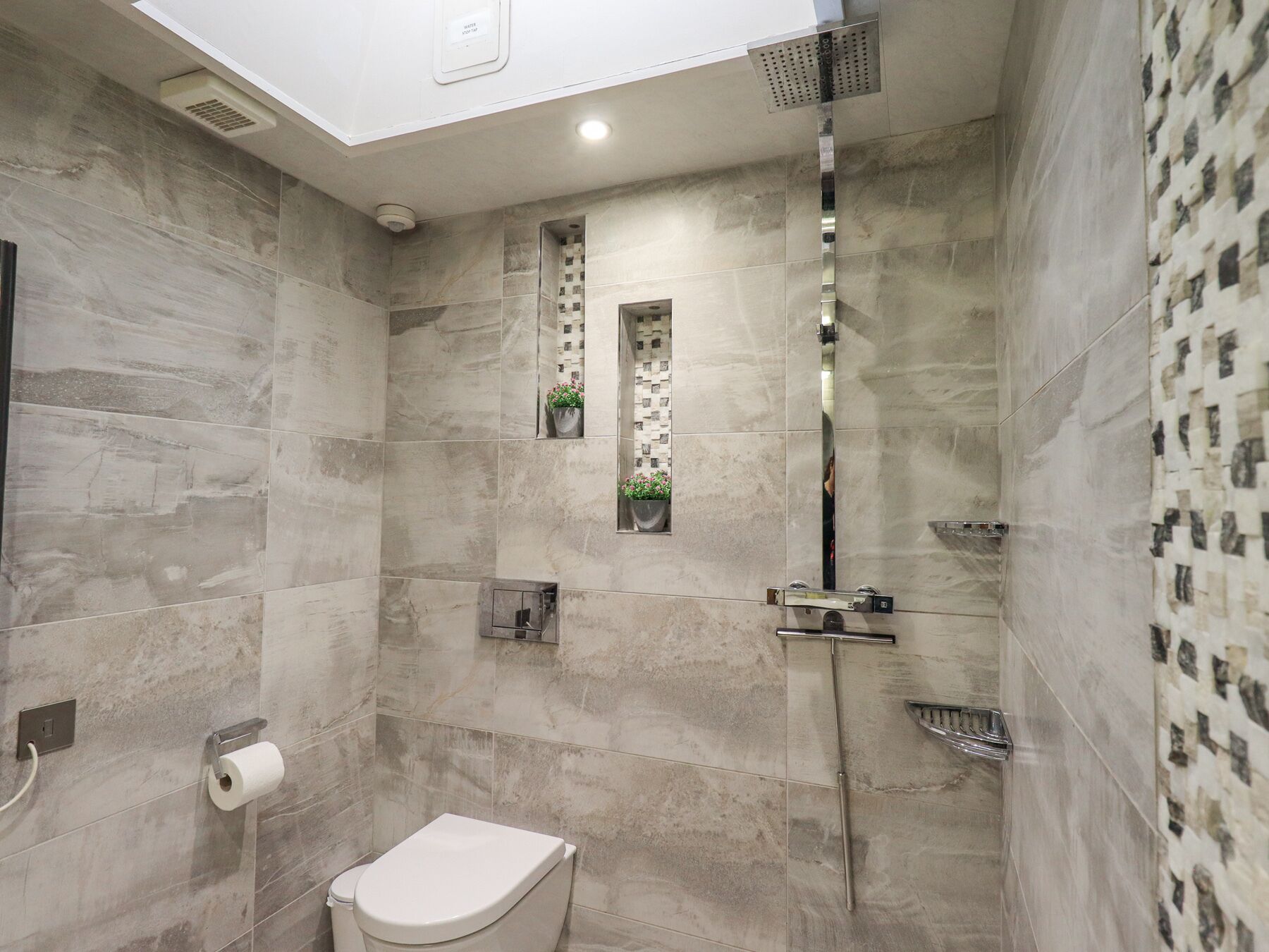 A modern bathroom with a toilet, shower, and a small window with a plant.