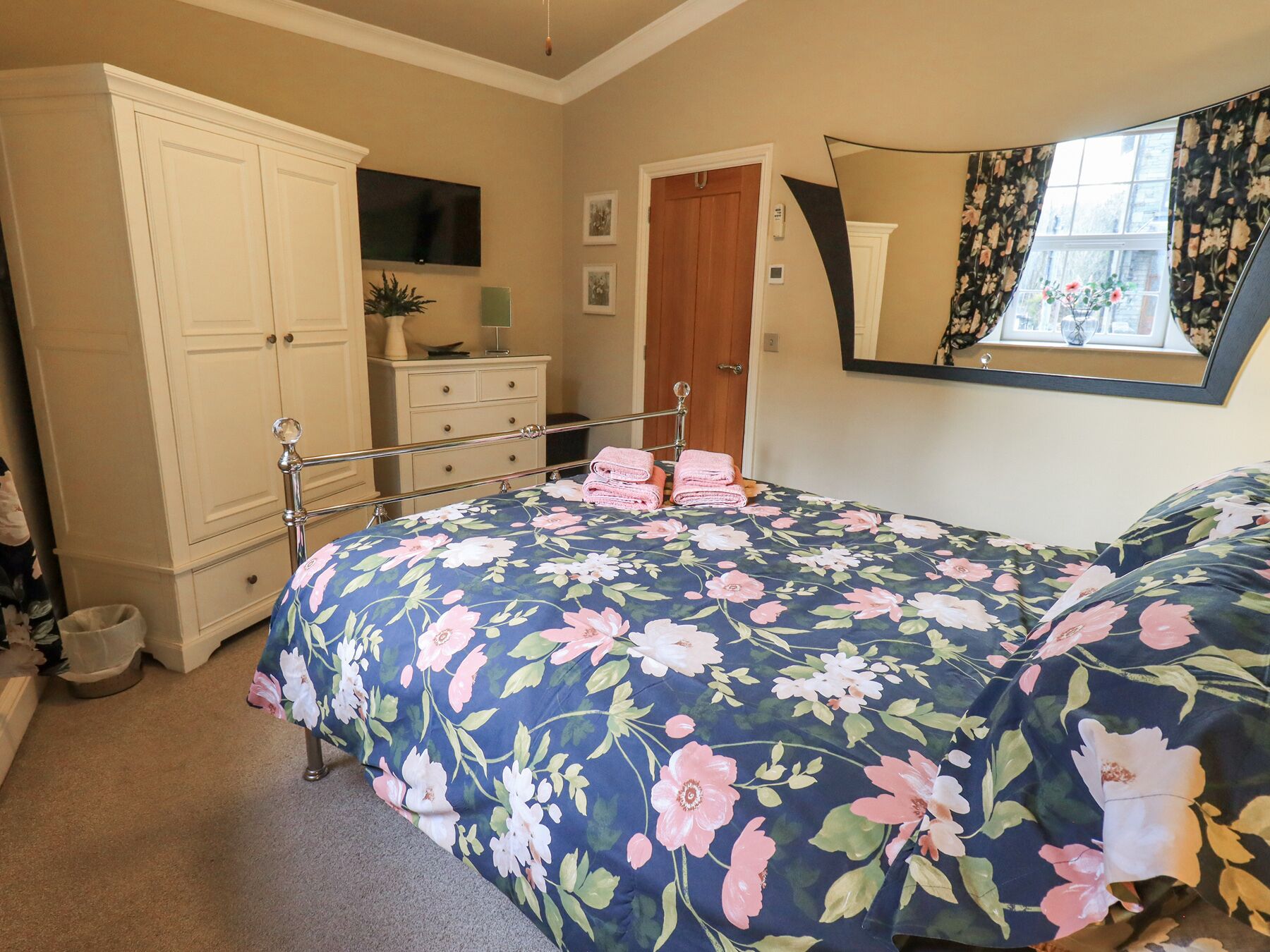 A bedroom with a bed, a dresser, a mirror, and a window with curtains.