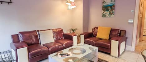 Una sala de estar con dos sofás de cuero, una mesa de centro de vidrio y una lámpara colgante.