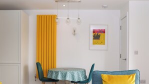 A dining area with a table and chairs, a yellow partition, and a framed picture on the wall. - Rolles Rainbow (Exmouth)