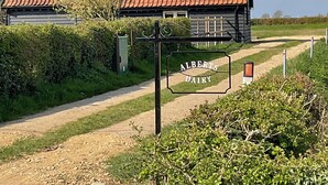 A rural road leading to a building with a red-tiled roof and a sign that reads 'ALBERTS DAIRY.' - Beautiful romantic converted barn located in a quiet setting. (Wingfield, near Diss)