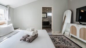 Ein Hotelzimmer mit Bett, Fernseher und einem sichtbaren Badezimmer hinter einer offenen Tür, sowie einem gemusterten Teppich.