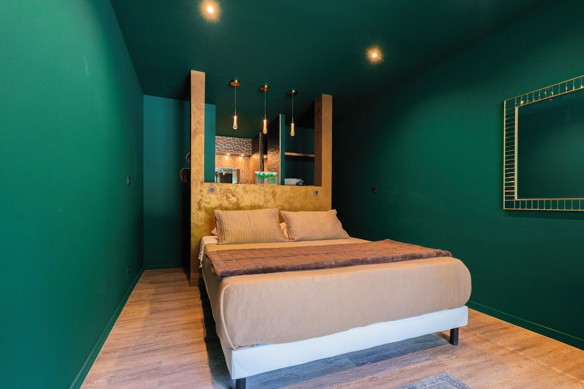 A bedroom with a bed, wooden floor, green walls, and pendant lights.