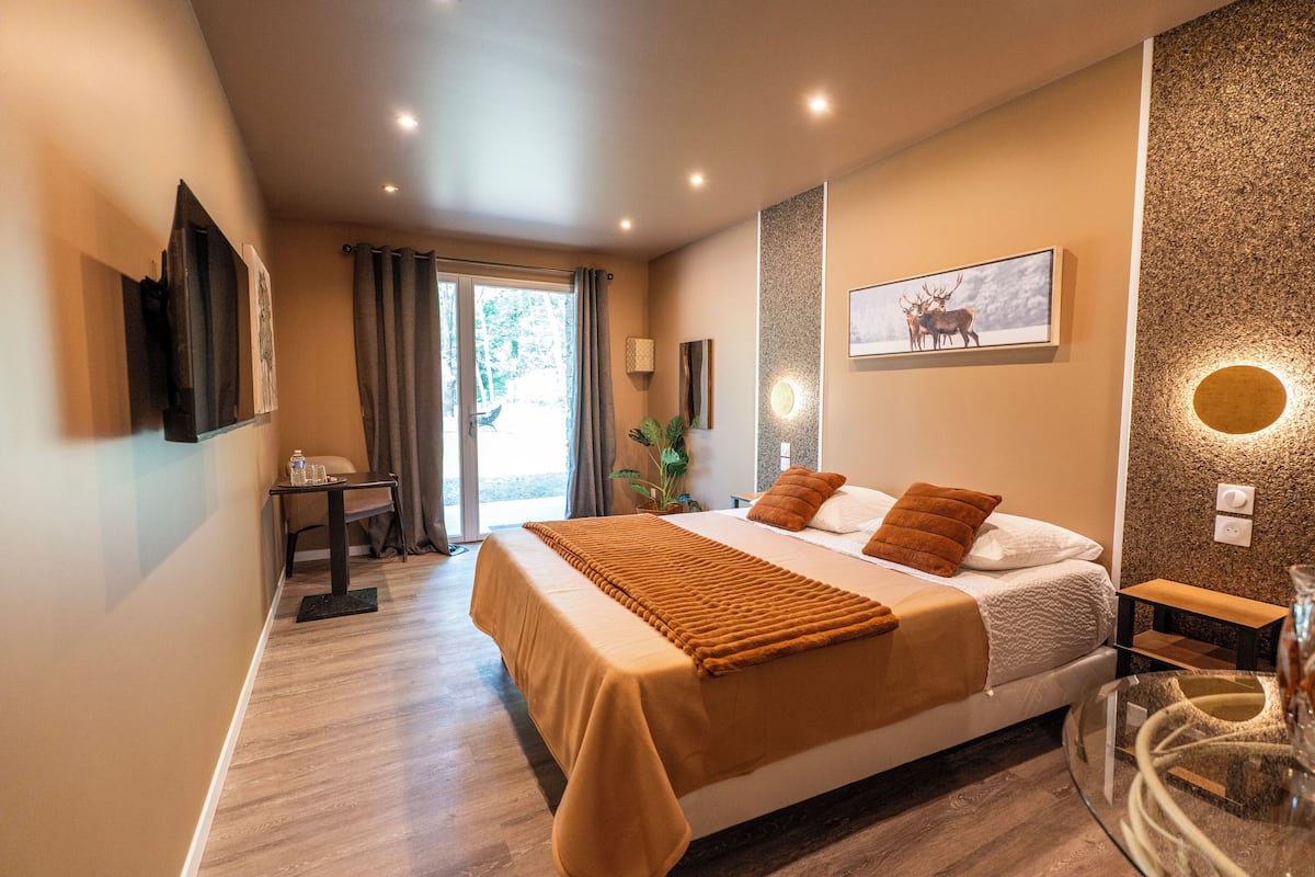 A modern hotel room with a large bed, a desk, and a glass table.