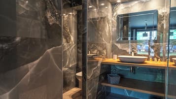 A modern bathroom with a marble wall, a large mirror, a wooden vanity, and a built-in sink.