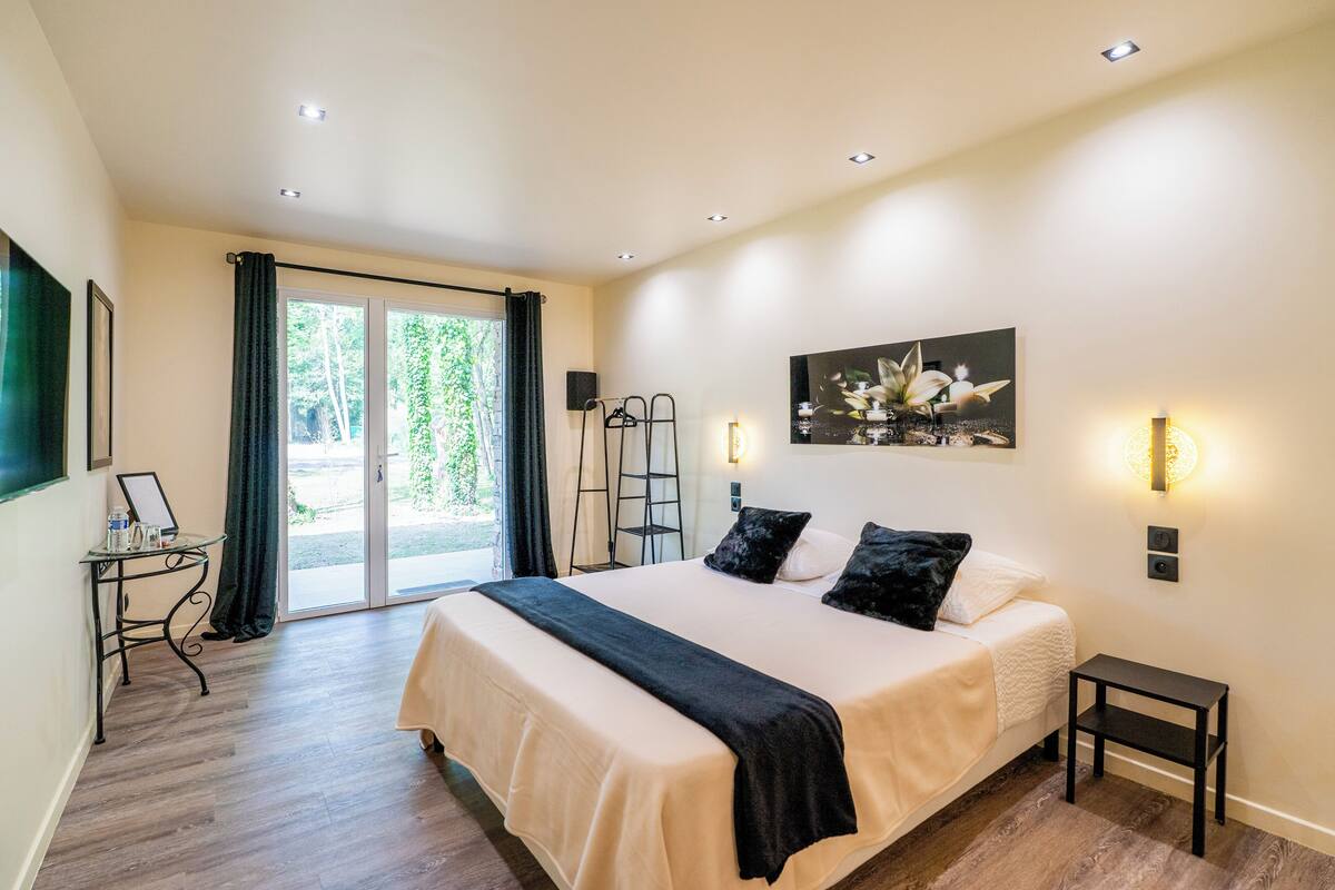 A bedroom with a large bed, a small table, a ladder, and a painting on the wall.