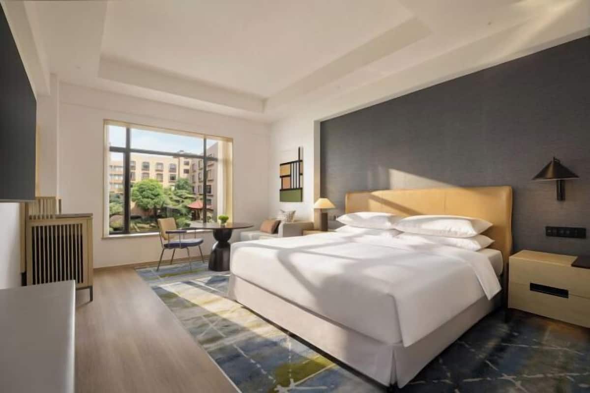 A modern hotel room with a large bed, bedside tables, a desk, and a view of the city.