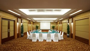 Un salón de conferencias con una larga mesa, sillas blancas y una pantalla para proyector.