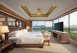 A spacious hotel room with a large bed, a television, a seating area, and a view of a cityscape through large windows. - Sheraton Guilin Hotel (Guilin)