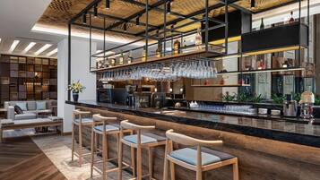 A modern bar area with a high ceiling, wooden bar stools, and a variety of bottles and glasses on shelves.