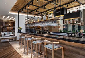 A modern bar area with a high ceiling, wooden bar stools, and a variety of bottles and glasses on shelves. - Sheraton Guilin Hotel (Guilin)