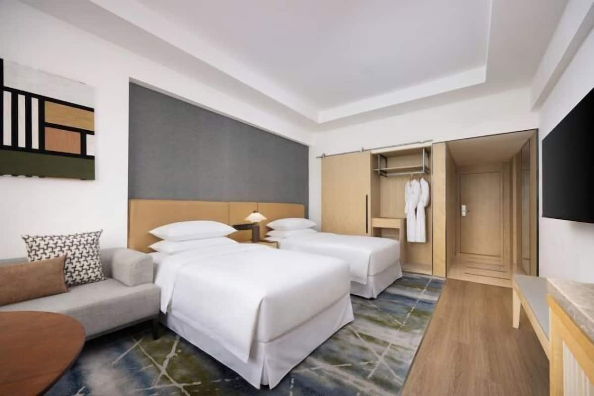 A hotel room with two beds, a sofa, a TV, a wardrobe, and a mirror.