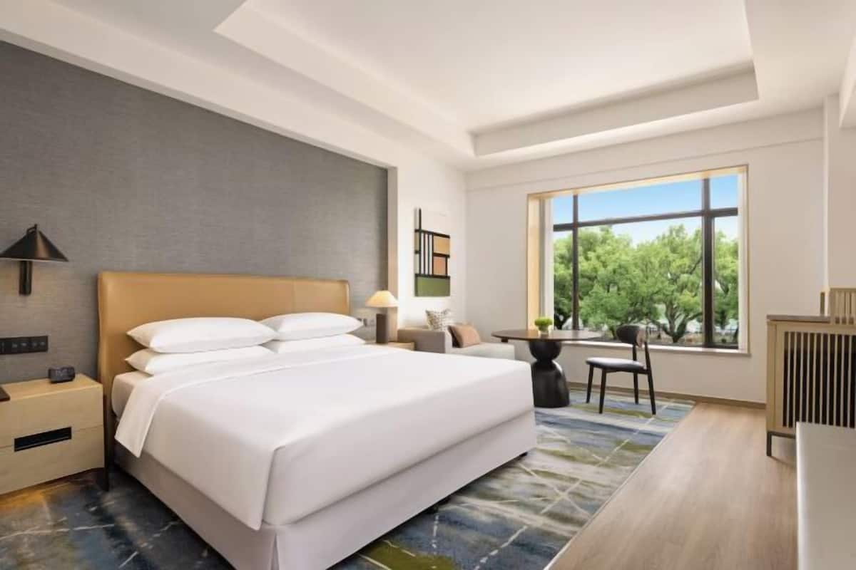 A hotel room with a large bed, bedside tables, a desk, and a window with a view.