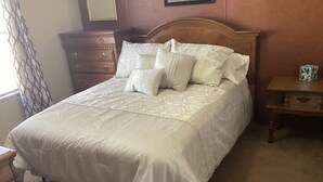 Un lit bien fait, avec une tête de lit en bois et une commode assortie placée à gauche.